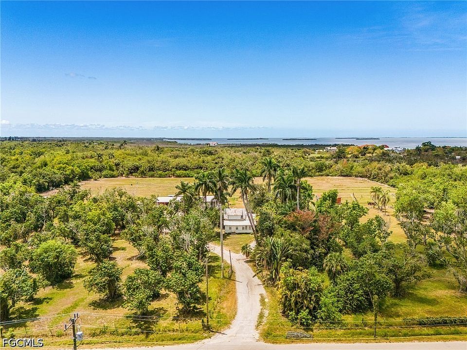 Long aerial perspective from the south showing the driveway leading north toward the homestead with the palm canopy and the bay behind it